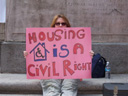 photo of a woman holding up a pink sign reading Housing Is A Civil Right