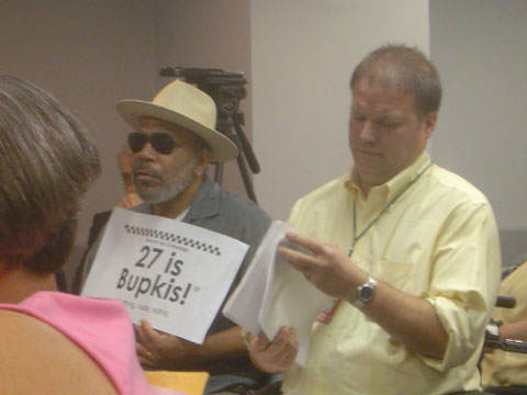 Photo of man, with Alexander Wood sitting next to him, holding sign reading 27 is bupkis