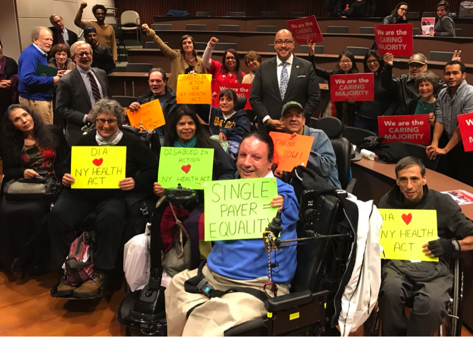 DIA members in City Hall in 2018 holding signs that endorse the NY Health Act. They are with Assemblymember Gottfried and NYS Senator Rivera.